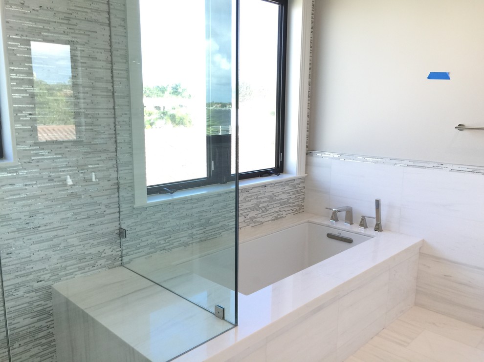 Design ideas for a mid-sized contemporary kids bathroom in Miami with an undermount sink, recessed-panel cabinets, white cabinets, marble benchtops, an undermount tub, a curbless shower, a one-piece toilet, gray tile, glass tile, grey walls and marble floors.