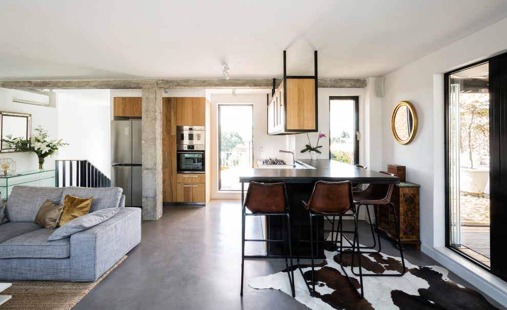 Contemporary open plan kitchen in Madrid with medium wood cabinets, concrete floors, with island, black benchtop, flat-panel cabinets and grey floor.