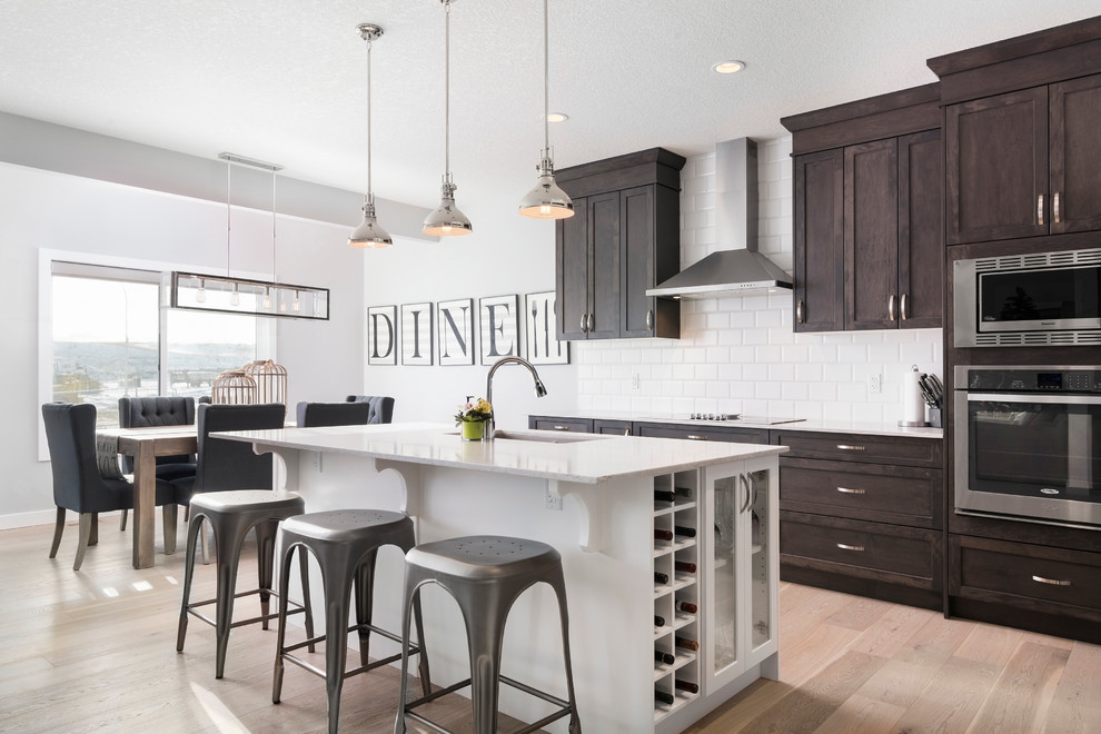 Inspiration for a transitional light wood floor kitchen remodel in Calgary with an undermount sink, shaker cabinets, dark wood cabinets, white backsplash, subway tile backsplash, stainless steel appliances and an island
