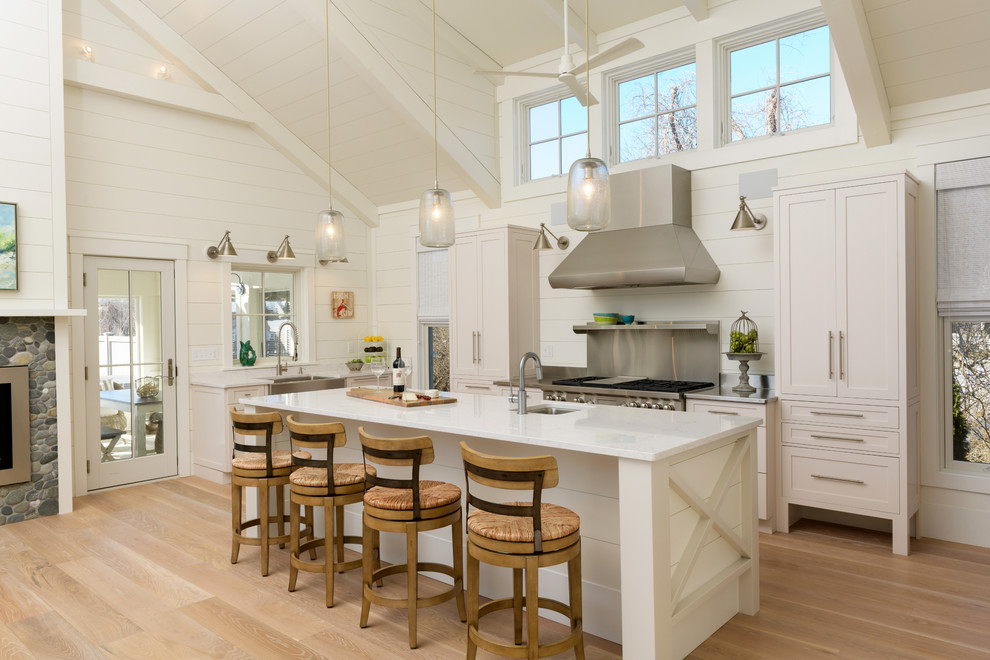 Photo of a beach style l-shaped open plan kitchen in Boston with an undermount sink, white cabinets, stainless steel appliances, medium hardwood floors, with island, brown floor, flat-panel cabinets, quartz benchtops, white splashback and timber splashback.