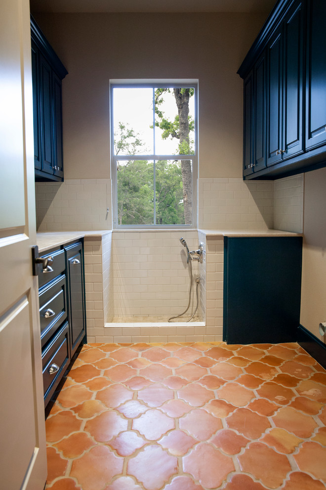 Photo of a mid-sized mediterranean u-shaped utility room in Dallas with raised-panel cabinets, blue cabinets, granite benchtops, beige walls, terra-cotta floors and a side-by-side washer and dryer.