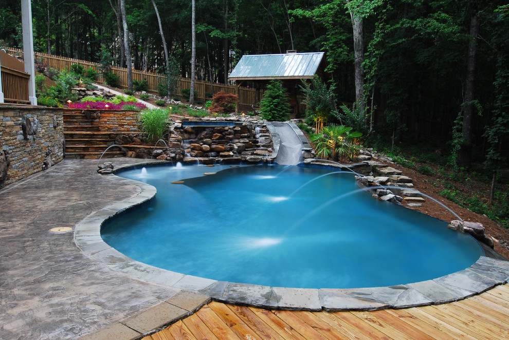 Large mountain style backyard kidney-shaped and stamped concrete infinity water slide photo in Atlanta