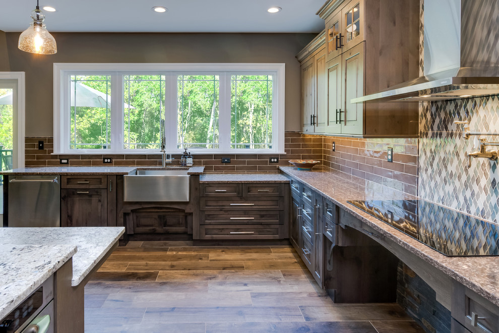 This is an example of a large country l-shaped open plan kitchen in Philadelphia with a farmhouse sink, raised-panel cabinets, distressed cabinets, quartz benchtops, grey splashback, cement tile splashback, stainless steel appliances, porcelain floors, with island and brown floor.