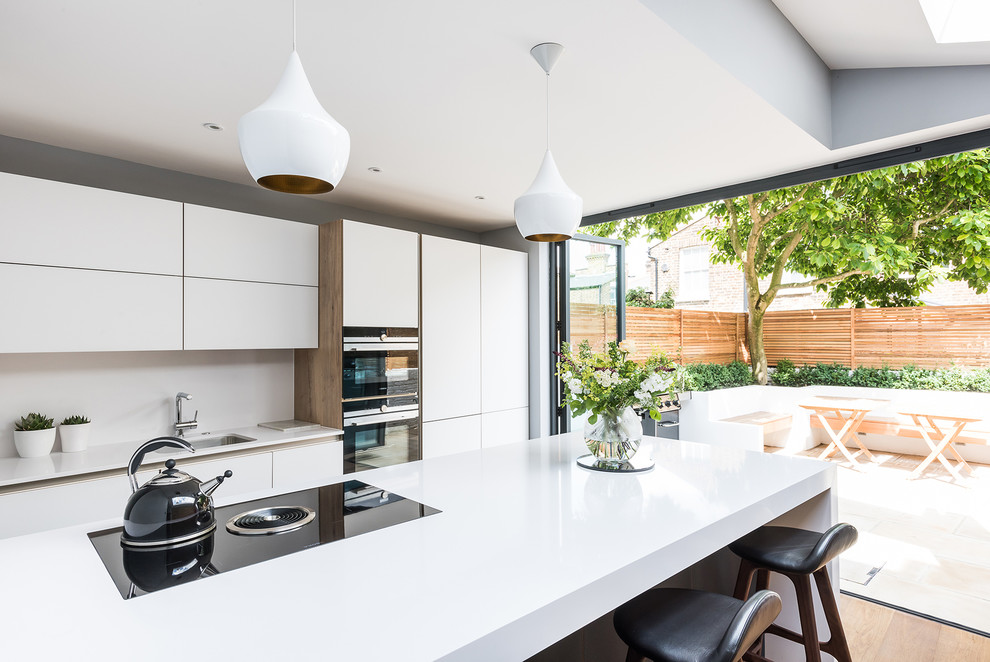 This is an example of a large contemporary single-wall open plan kitchen in London with flat-panel cabinets, white cabinets, with island, medium hardwood floors, white splashback, stainless steel appliances and an undermount sink.