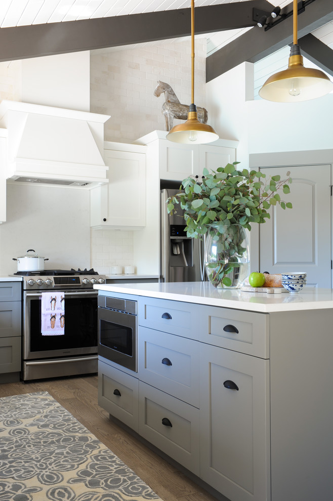 This is an example of a mid-sized transitional u-shaped eat-in kitchen in Other with shaker cabinets, stainless steel appliances, with island, a farmhouse sink, solid surface benchtops, beige splashback, brick splashback, light hardwood floors and brown floor.