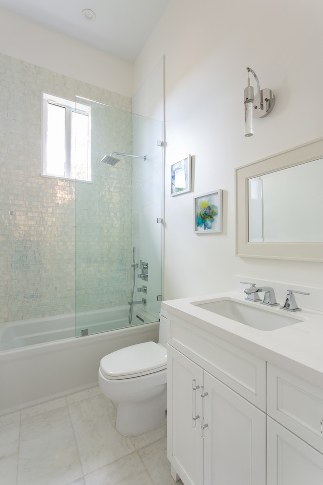 Photo of a mid-sized beach style master bathroom in Miami with recessed-panel cabinets, white cabinets, an alcove tub, a shower/bathtub combo, a two-piece toilet, white walls, porcelain floors, an undermount sink and solid surface benchtops.