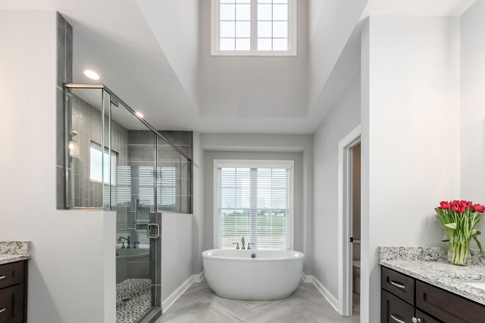 Inspiration for a transitional master bathroom in Columbus with recessed-panel cabinets, dark wood cabinets, a freestanding tub, an alcove shower, gray tile, an undermount sink, grey floor, a hinged shower door and grey benchtops.