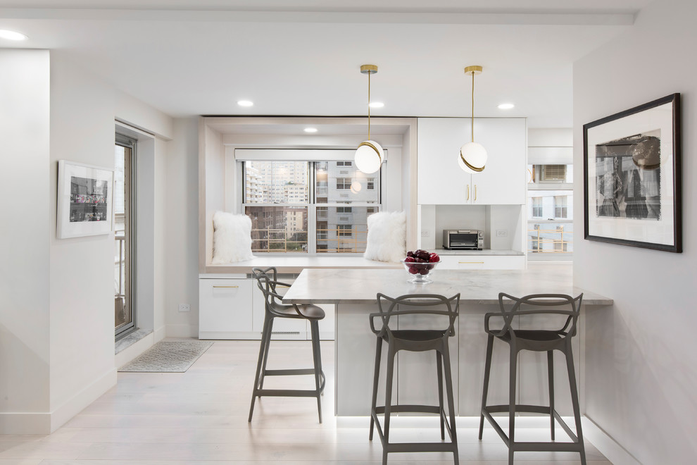 Large contemporary l-shaped open plan kitchen in New York with flat-panel cabinets, marble benchtops, white cabinets, a peninsula, white floor, white benchtop, stainless steel appliances and light hardwood floors.