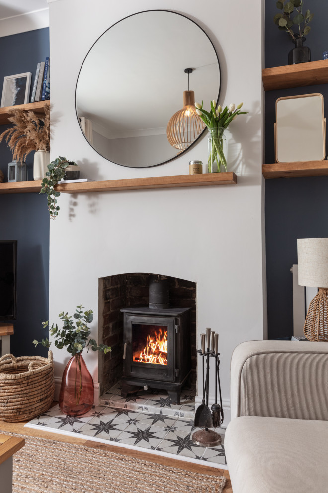 Inspiration for a mid-sized scandinavian formal open concept living room in Cornwall with blue walls, medium hardwood floors, a wood stove, a plaster fireplace surround, a corner tv and brown floor.
