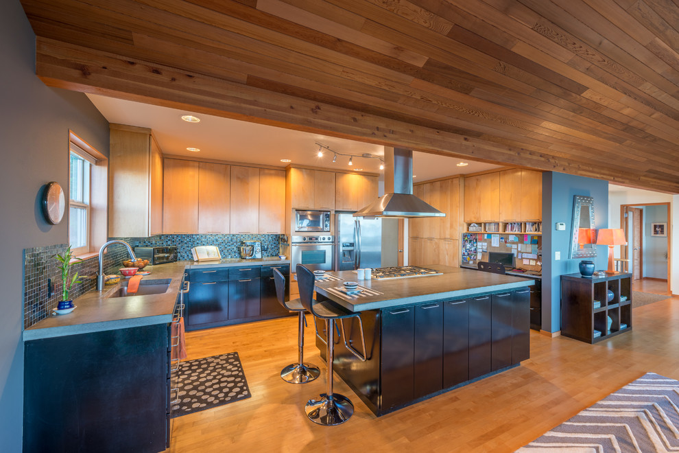 This is an example of a contemporary u-shaped kitchen in Seattle with an undermount sink, flat-panel cabinets, medium wood cabinets, blue splashback, mosaic tile splashback, stainless steel appliances, medium hardwood floors, with island, brown floor and grey benchtop.