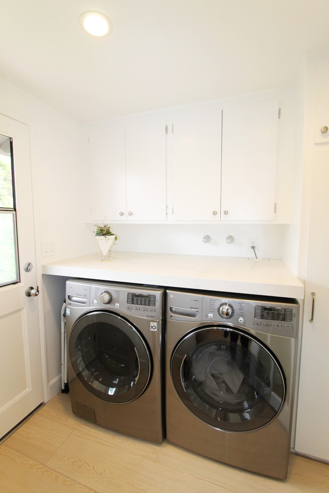 Inspiration for a small single-wall laundry room in Los Angeles with flat-panel cabinets, white cabinets, white splashback, white walls, light hardwood floors, a side-by-side washer and dryer, beige floor, white benchtop and vaulted.