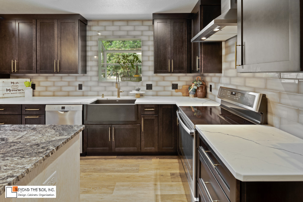 Kitchen - mid-sized transitional l-shaped medium tone wood floor and brown floor kitchen idea with a farmhouse sink, shaker cabinets, black cabinets, granite countertops, gray backsplash, ceramic backsplash, stainless steel appliances, an island and white countertops