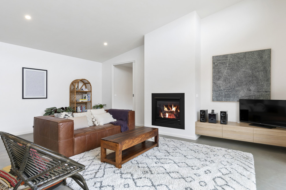 Photo of a small beach style open concept family room in Geelong with concrete floors, a standard fireplace, a plaster fireplace surround, a freestanding tv and grey floor.
