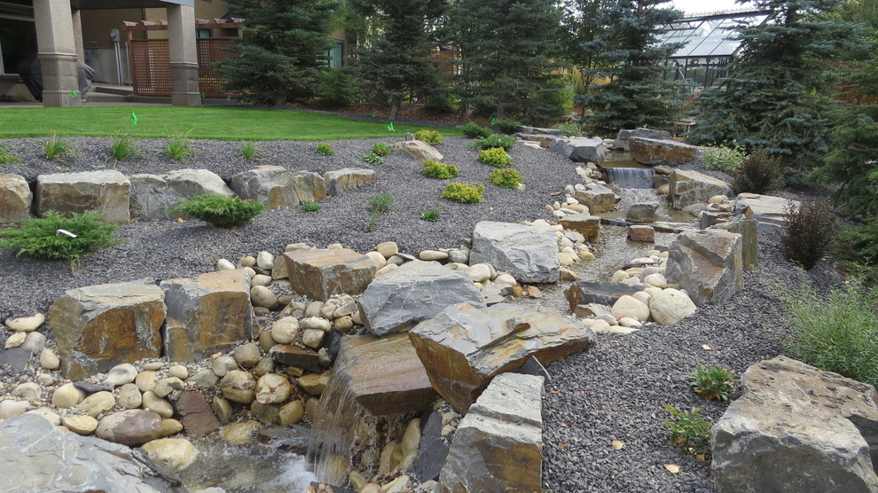 Design ideas for a large transitional backyard formal garden in Calgary with with pond and gravel.