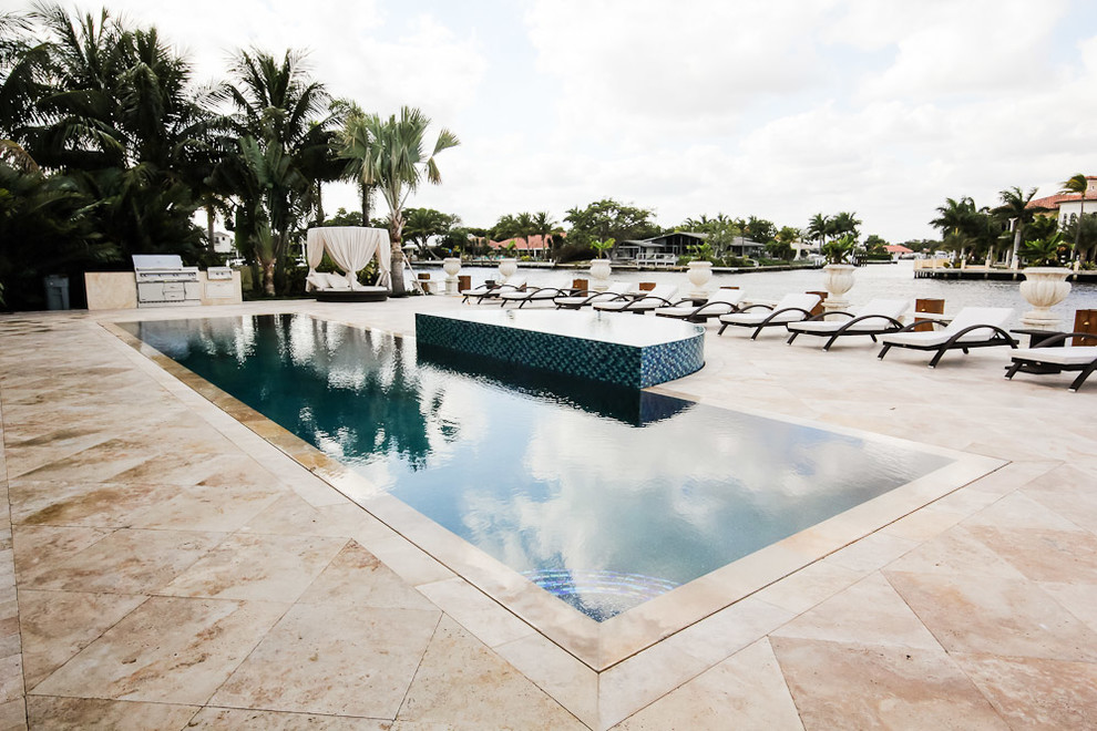 This is an example of a large backyard rectangular lap pool in Miami with a hot tub and natural stone pavers.