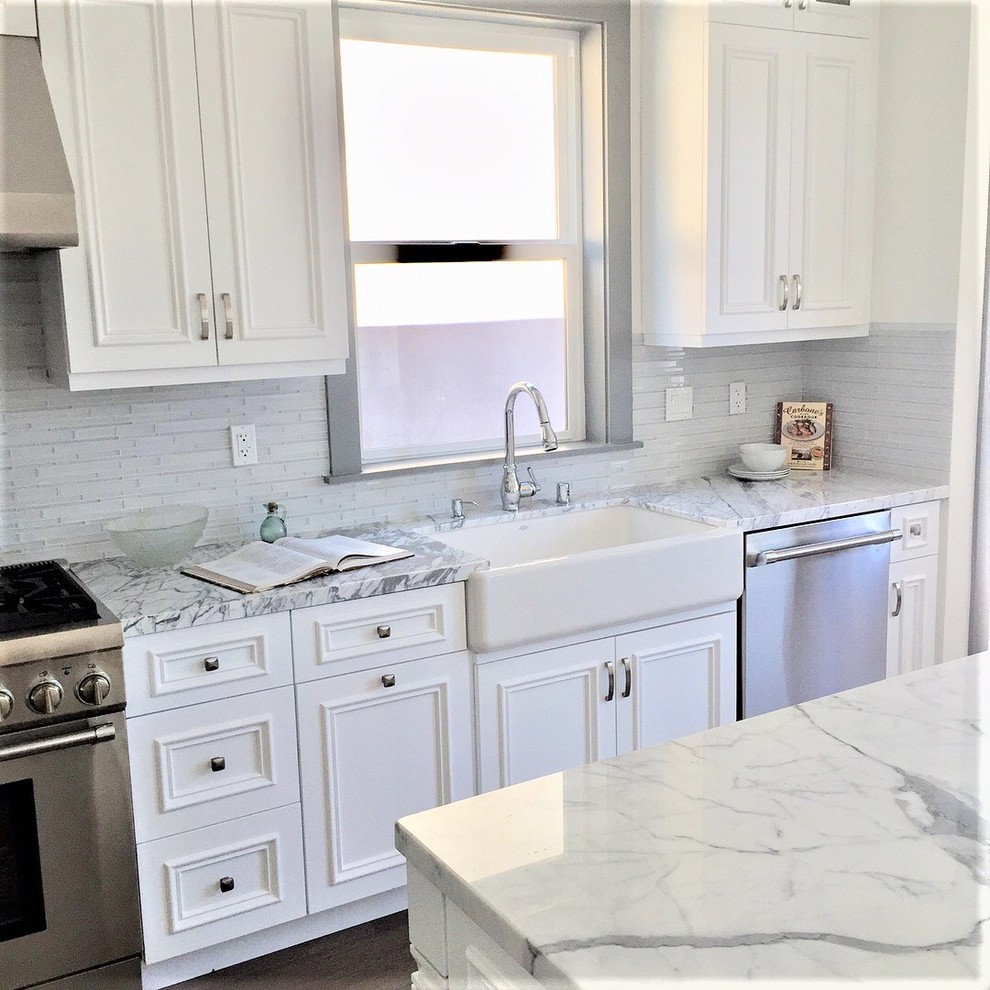 Photo of a large modern l-shaped eat-in kitchen in Seattle with a farmhouse sink, beaded inset cabinets, white cabinets, marble benchtops, grey splashback, ceramic splashback, stainless steel appliances, medium hardwood floors, with island and grey benchtop.