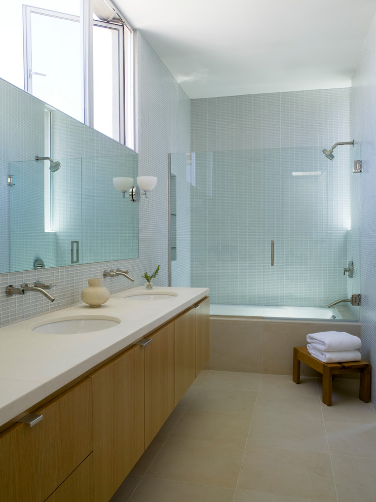 Photo of a mid-sized contemporary master bathroom in Los Angeles with flat-panel cabinets, medium wood cabinets, an undermount tub, a shower/bathtub combo, glass tile, porcelain floors, an undermount sink, engineered quartz benchtops, a hinged shower door, blue tile, beige floor and white walls.