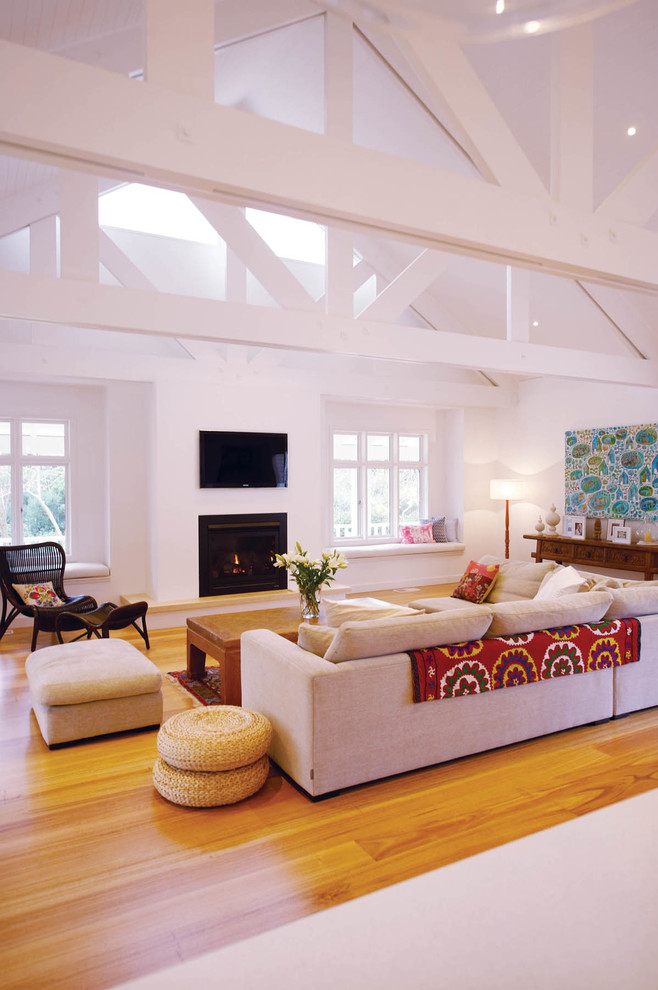 This is an example of a large beach style open concept living room in Melbourne with white walls, medium hardwood floors, a standard fireplace and a wall-mounted tv.