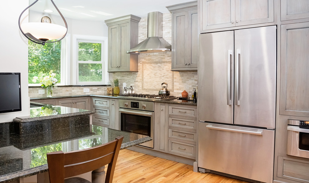 This is an example of a transitional kitchen in New York with grey cabinets, marble benchtops, beige splashback, subway tile splashback, stainless steel appliances and light hardwood floors.