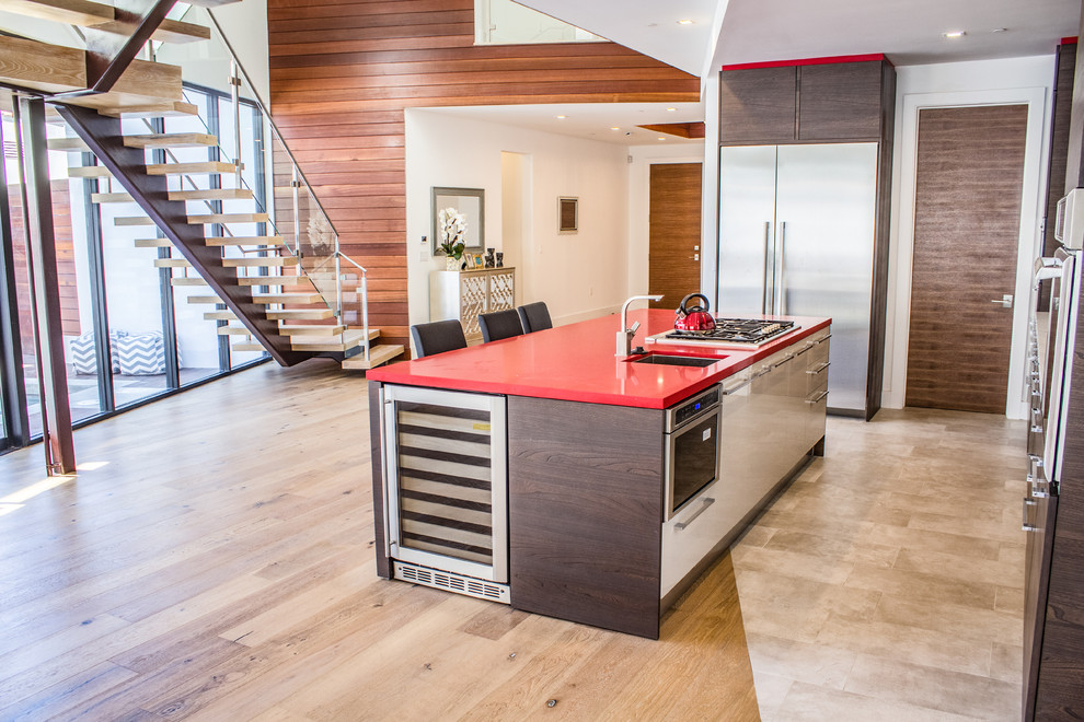 Photo of a mid-sized contemporary single-wall eat-in kitchen in Los Angeles with an undermount sink, flat-panel cabinets, dark wood cabinets, solid surface benchtops, white splashback, stainless steel appliances, light hardwood floors, with island, brown floor and red benchtop.