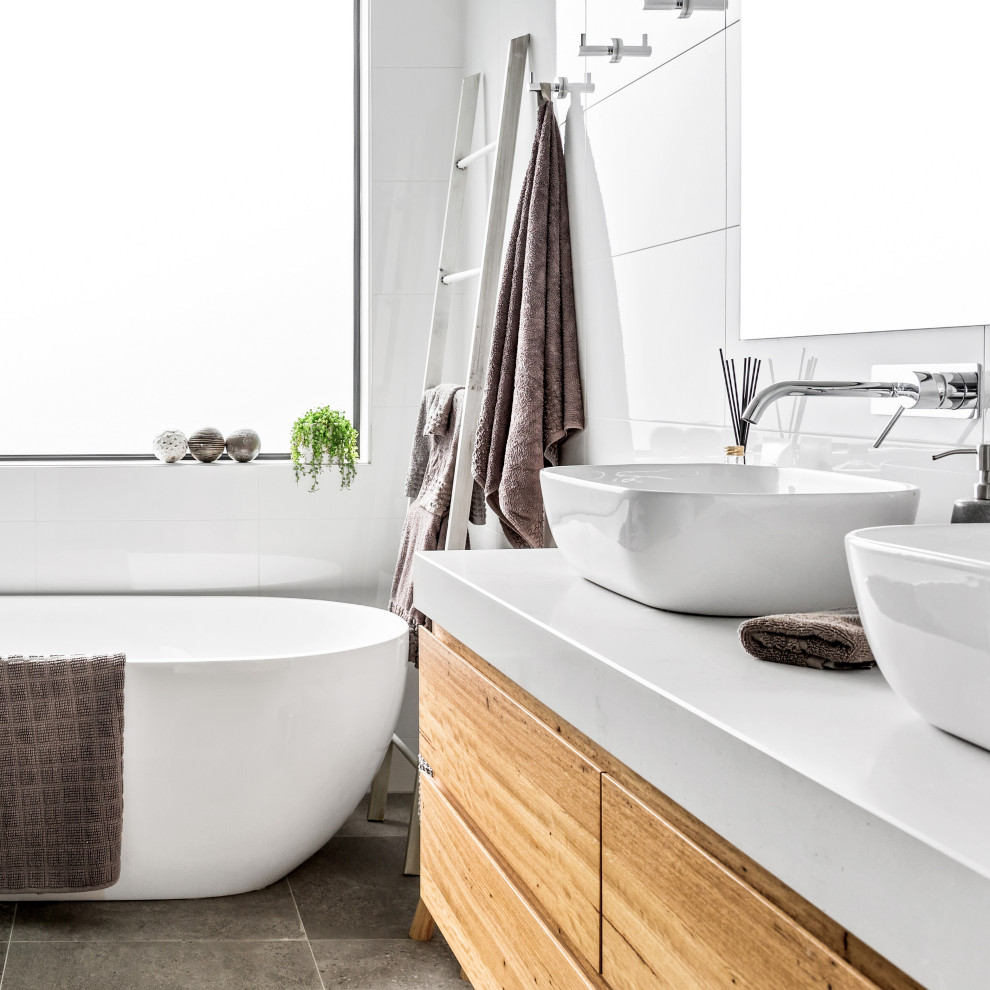 This is an example of a contemporary bathroom in Melbourne with flat-panel cabinets, medium wood cabinets, a freestanding tub, white tile, a vessel sink, grey floor, white benchtops, a double vanity and a floating vanity.