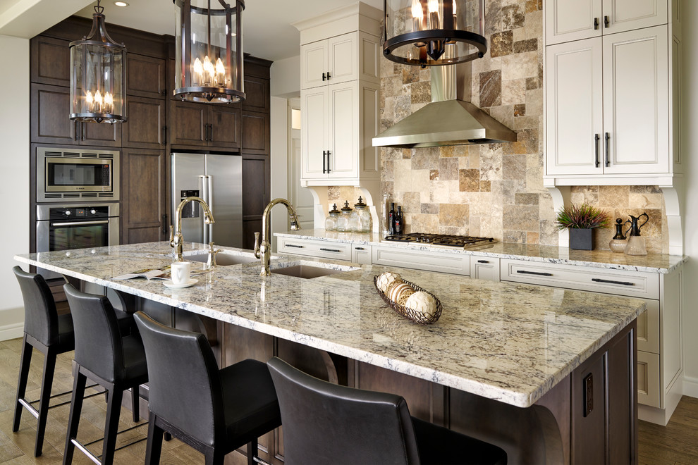 Inspiration for a transitional galley medium tone wood floor open concept kitchen remodel in Calgary with an undermount sink, beaded inset cabinets, white cabinets, granite countertops, beige backsplash, stone tile backsplash, stainless steel appliances and an island