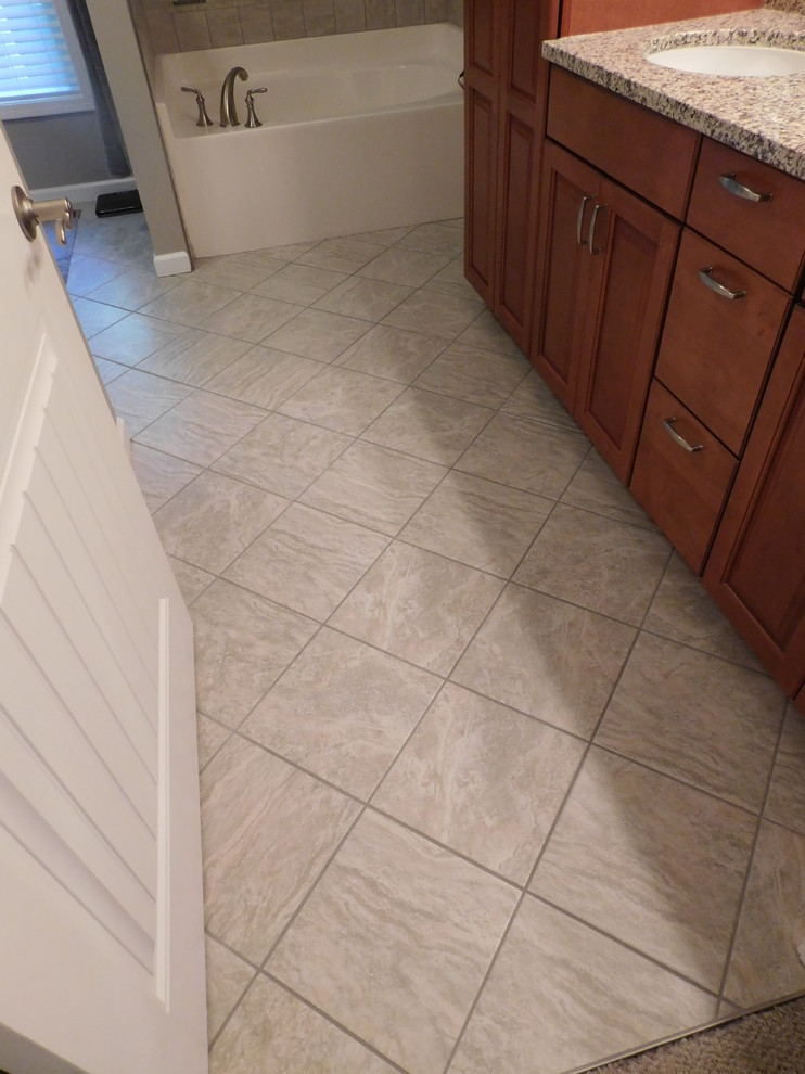 Large transitional master gray tile and ceramic tile ceramic tile corner bathtub photo with raised-panel cabinets, medium tone wood cabinets, a two-piece toilet, beige walls, an undermount sink and granite countertops