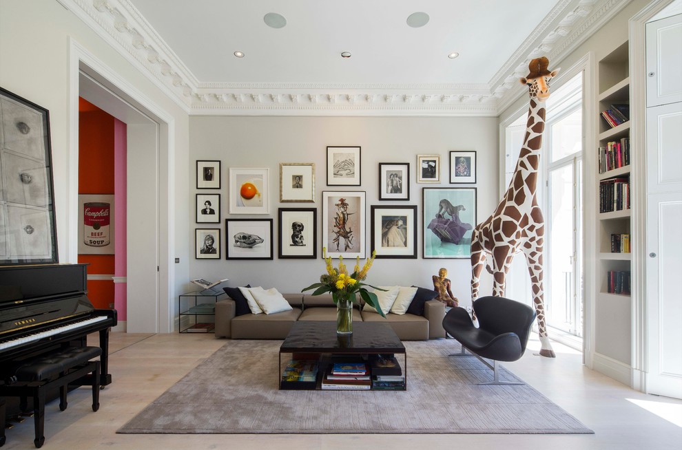 This is an example of an eclectic enclosed living room in London with a library, grey walls and light hardwood floors.