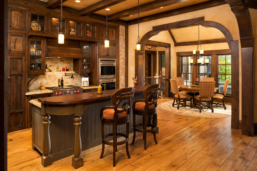 This is an example of a large traditional galley eat-in kitchen in Minneapolis with glass-front cabinets, dark wood cabinets, wood benchtops, beige splashback, stone tile splashback, stainless steel appliances, a farmhouse sink, medium hardwood floors and with island.