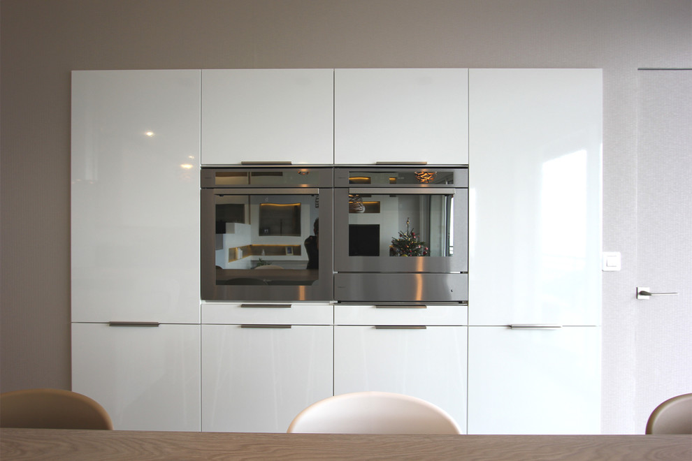 Photo of a mid-sized contemporary u-shaped eat-in kitchen in Lyon with an undermount sink, flat-panel cabinets, white cabinets, laminate benchtops, white splashback, glass sheet splashback, stainless steel appliances, laminate floors, with island, beige benchtop and grey floor.