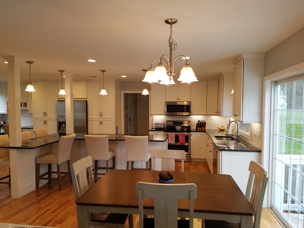 Large transitional l-shaped light wood floor and brown floor eat-in kitchen photo with an undermount sink, shaker cabinets, white cabinets, granite countertops, white backsplash, subway tile backsplash, stainless steel appliances and an island