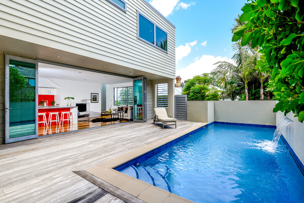 Large contemporary backyard rectangular pool in Auckland with a water feature and decking.