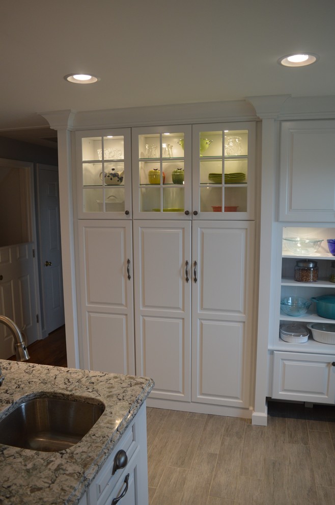 Example of a large transitional u-shaped ceramic tile and gray floor home design design with a farmhouse sink, raised-panel cabinets, white cabinets, quartz countertops, gray backsplash, glass tile backsplash, stainless steel appliances and an island