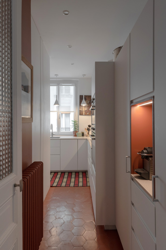 Bild på ett avskilt, litet funkis beige beige l-kök, med en undermonterad diskho, släta luckor, vita skåp, bänkskiva i kvarts, rött stänkskydd, stänkskydd i mosaik, integrerade vitvaror, cementgolv och rött golv