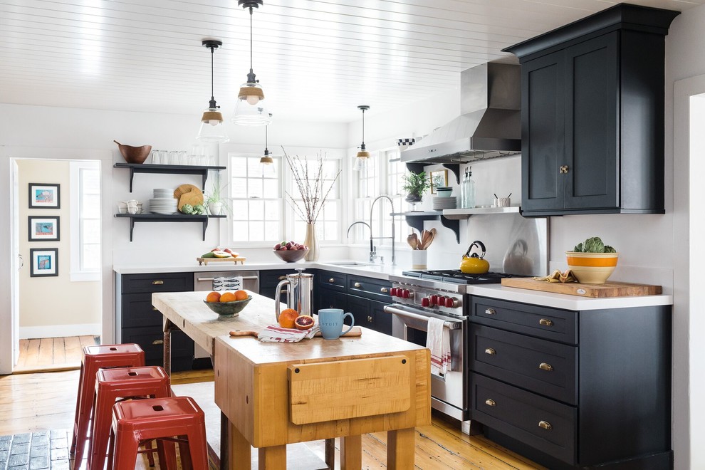 Inspiration for a beach style l-shaped kitchen in Boston with shaker cabinets, black cabinets, stainless steel appliances, light hardwood floors, with island, beige floor and white benchtop.