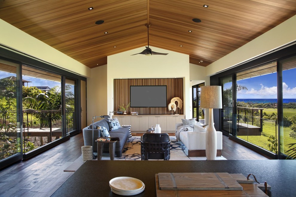 This is an example of a large tropical open concept living room in Hawaii with beige walls and brown floor.