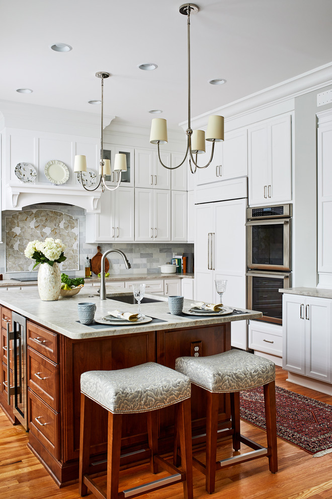 Inspiration for a large traditional l-shaped kitchen in DC Metro with white cabinets, grey splashback, medium hardwood floors, with island, grey benchtop, an undermount sink, recessed-panel cabinets, stainless steel appliances and brown floor.