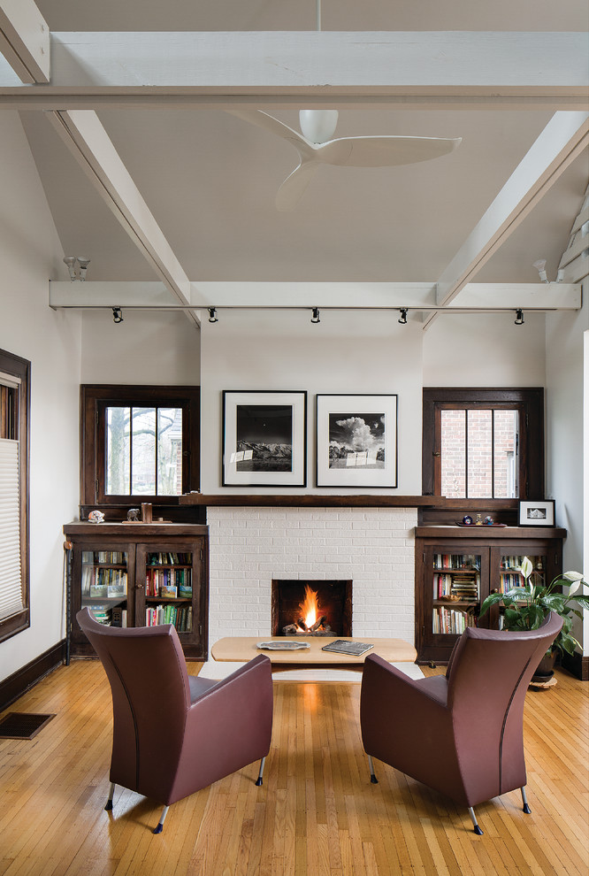 This is an example of a small contemporary open concept living room in Indianapolis with light hardwood floors, a standard fireplace, a brick fireplace surround, a built-in media wall and white walls.