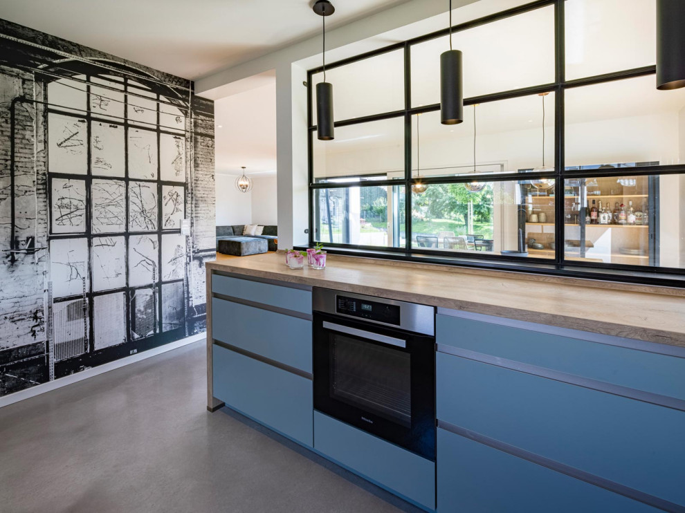 На фото: отдельная, п-образная кухня в стиле лофт с синими фасадами, деревянной столешницей и обоями на стенах без острова