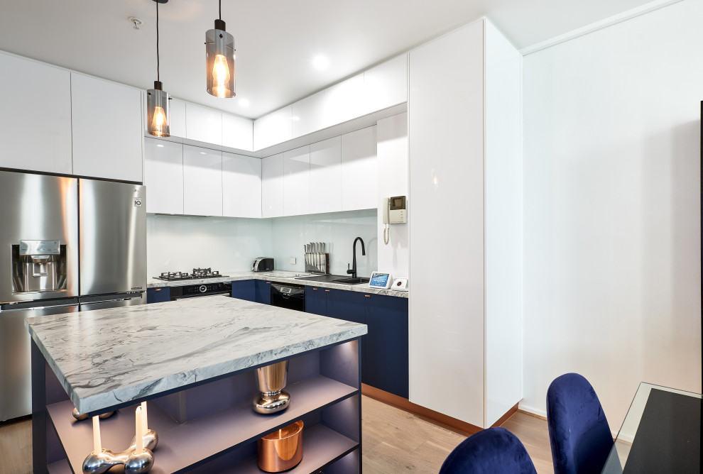 Inspiration for a small contemporary l-shaped kitchen pantry in Melbourne with a drop-in sink, flat-panel cabinets, blue cabinets, quartz benchtops, white splashback, glass sheet splashback, stainless steel appliances, medium hardwood floors, with island, beige floor and white benchtop.