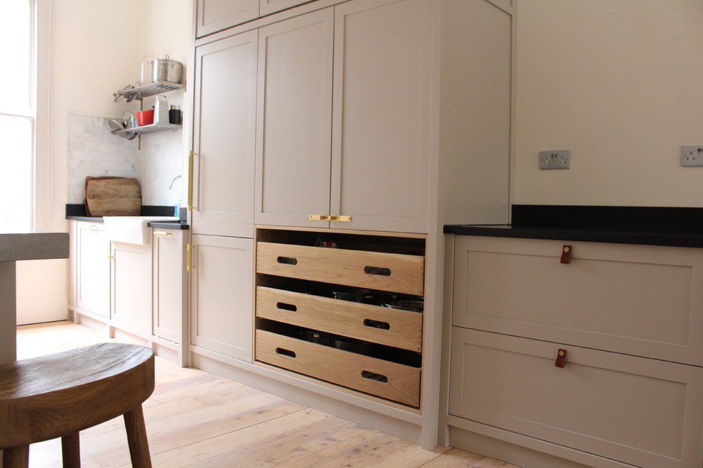 Large arts and crafts single-wall open plan kitchen in London with a farmhouse sink, shaker cabinets, medium wood cabinets, concrete benchtops, black splashback, slate splashback, panelled appliances, light hardwood floors, with island and multi-coloured floor.