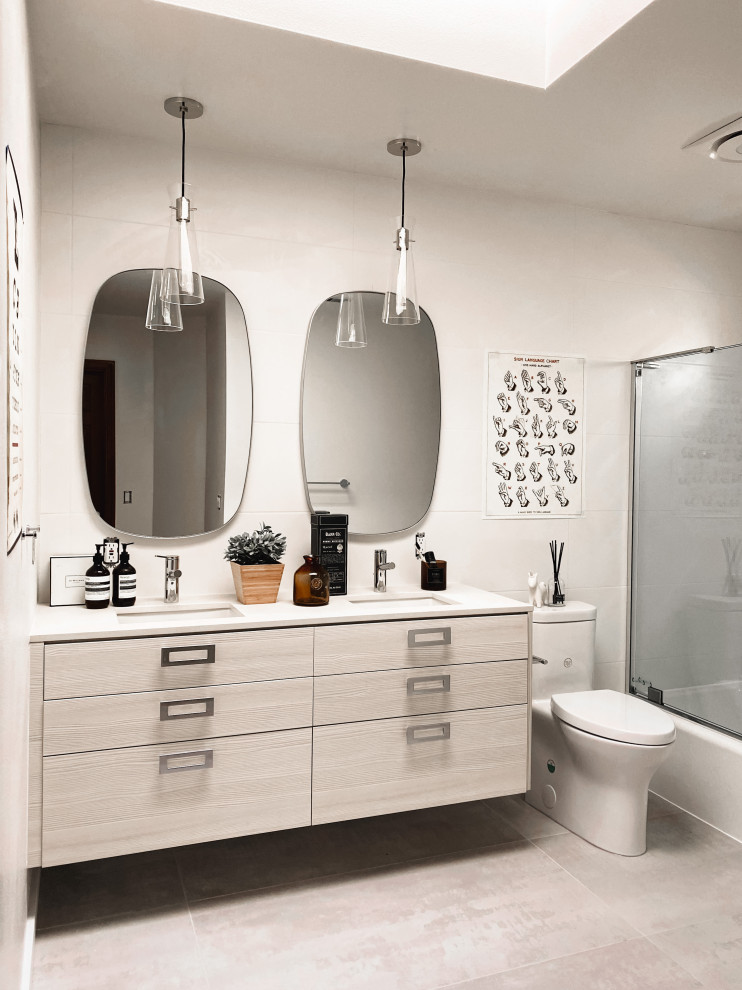 Design ideas for a mid-sized modern kids bathroom in Seattle with flat-panel cabinets, light wood cabinets, a drop-in tub, a shower/bathtub combo, a one-piece toilet, white tile, porcelain tile, white walls, porcelain floors, an undermount sink, quartzite benchtops, grey floor, a hinged shower door, beige benchtops, a niche, a double vanity, a floating vanity and vaulted.