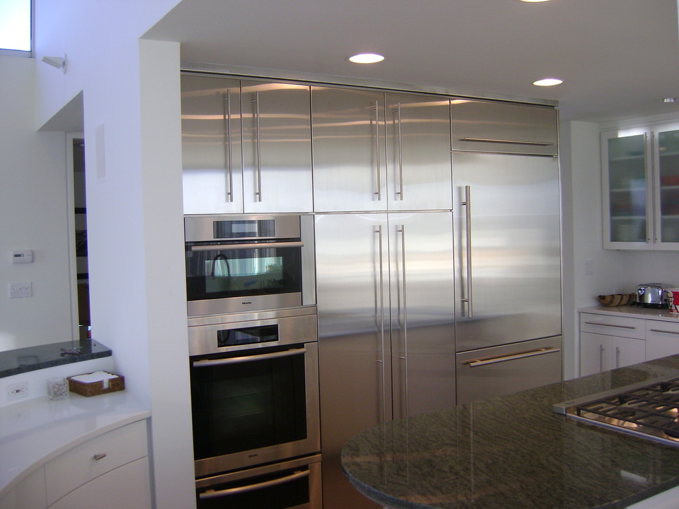 This is an example of a mid-sized modern single-wall eat-in kitchen in Orange County with flat-panel cabinets, stainless steel cabinets, granite benchtops, stainless steel appliances, with island and white splashback.