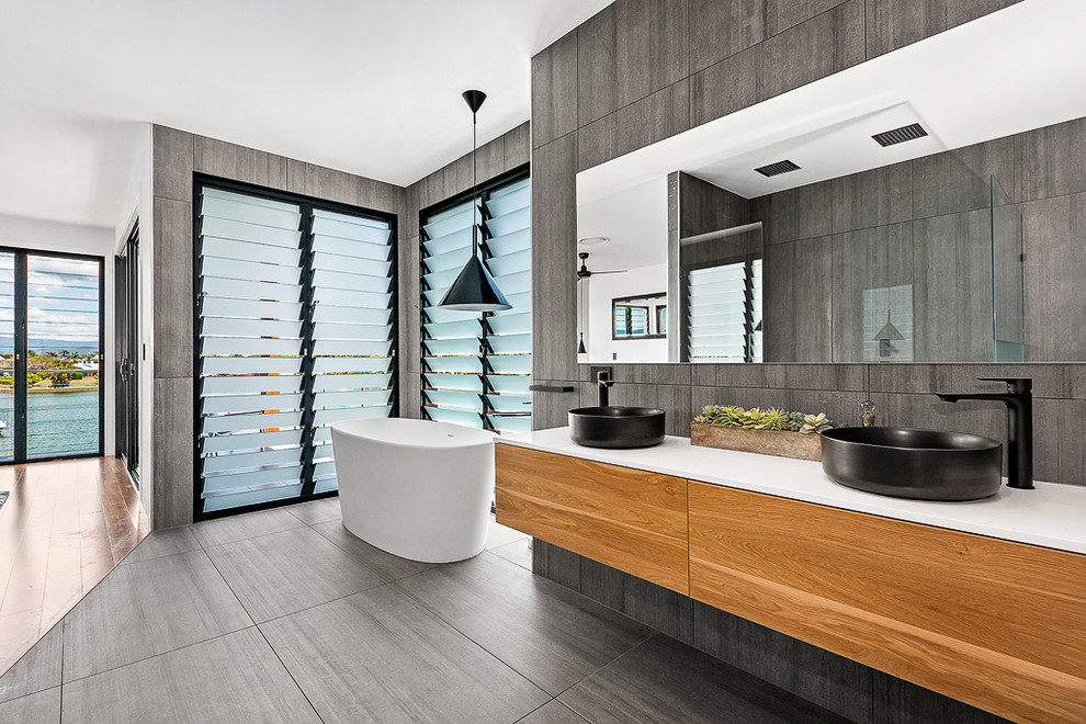 Contemporary master bathroom in Brisbane with a freestanding tub, porcelain tile, porcelain floors, grey floor, flat-panel cabinets, medium wood cabinets, grey walls, a vessel sink and gray tile.