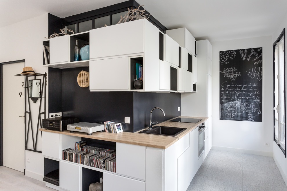 Design ideas for a mid-sized modern single-wall open plan kitchen in Paris with wood benchtops, a drop-in sink, flat-panel cabinets, white cabinets, black splashback, slate splashback, black appliances, vinyl floors, no island, grey floor and beige benchtop.