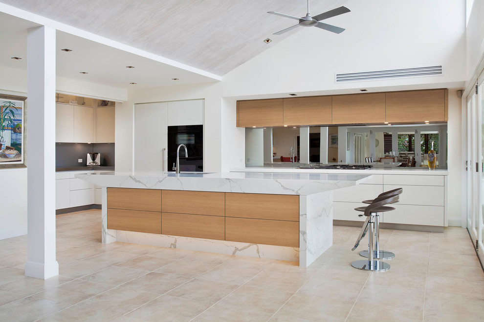 Design ideas for a large contemporary l-shaped open plan kitchen in Sydney with an undermount sink, flat-panel cabinets, white cabinets, quartz benchtops, grey splashback, mirror splashback, black appliances, limestone floors and with island.