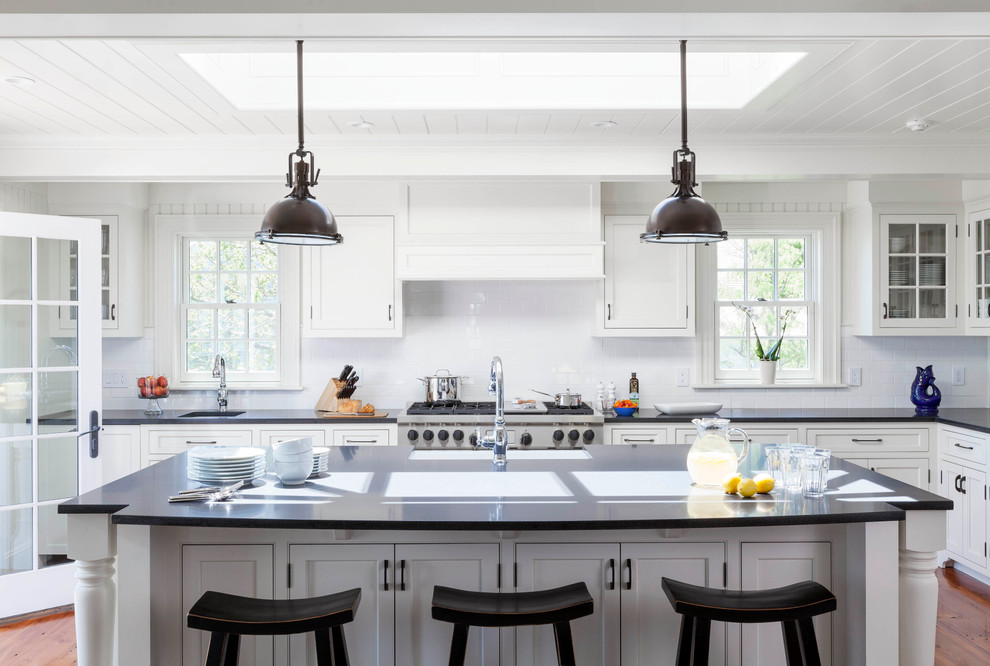 Inspiration for a large beach style galley kitchen in Boston with an undermount sink, shaker cabinets, white cabinets, solid surface benchtops, white splashback, subway tile splashback, stainless steel appliances, medium hardwood floors, with island and brown floor.