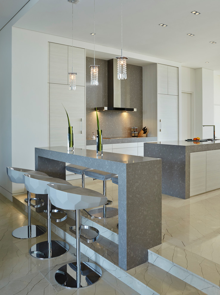 Expansive contemporary galley open plan kitchen in Miami with flat-panel cabinets, white cabinets, quartzite benchtops, grey splashback, panelled appliances, marble floors, multiple islands and stone slab splashback.