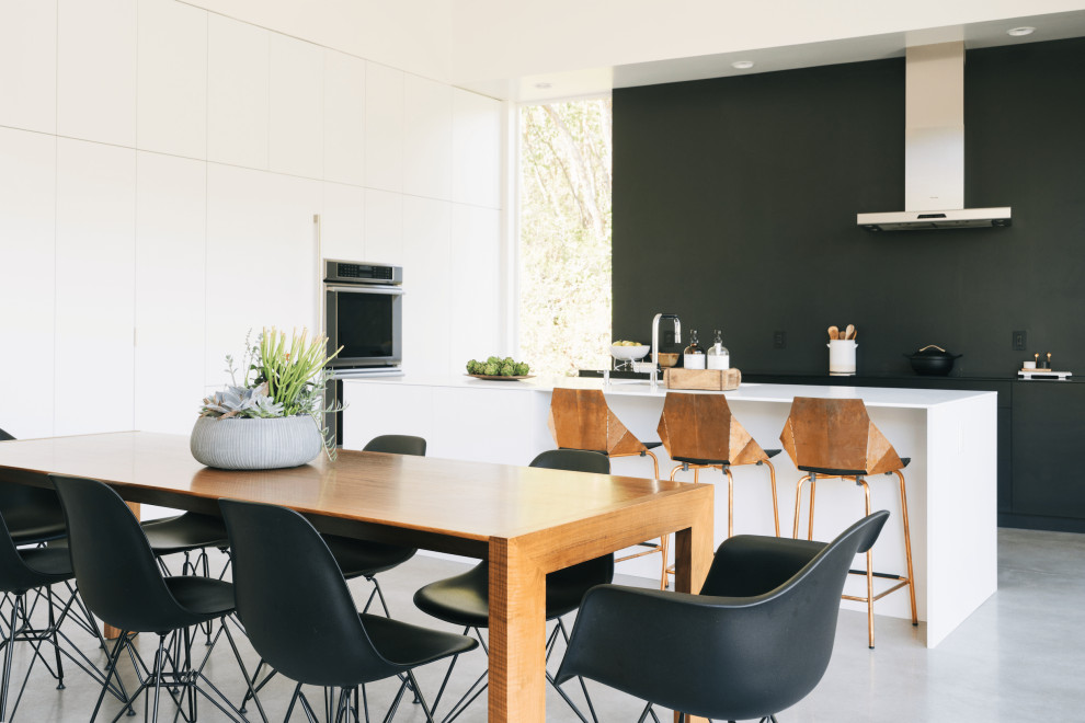 Inspiration for an expansive modern kitchen in Salt Lake City with an undermount sink, flat-panel cabinets, white cabinets, solid surface benchtops, black splashback, panelled appliances, concrete floors, with island, grey floor and white benchtop.