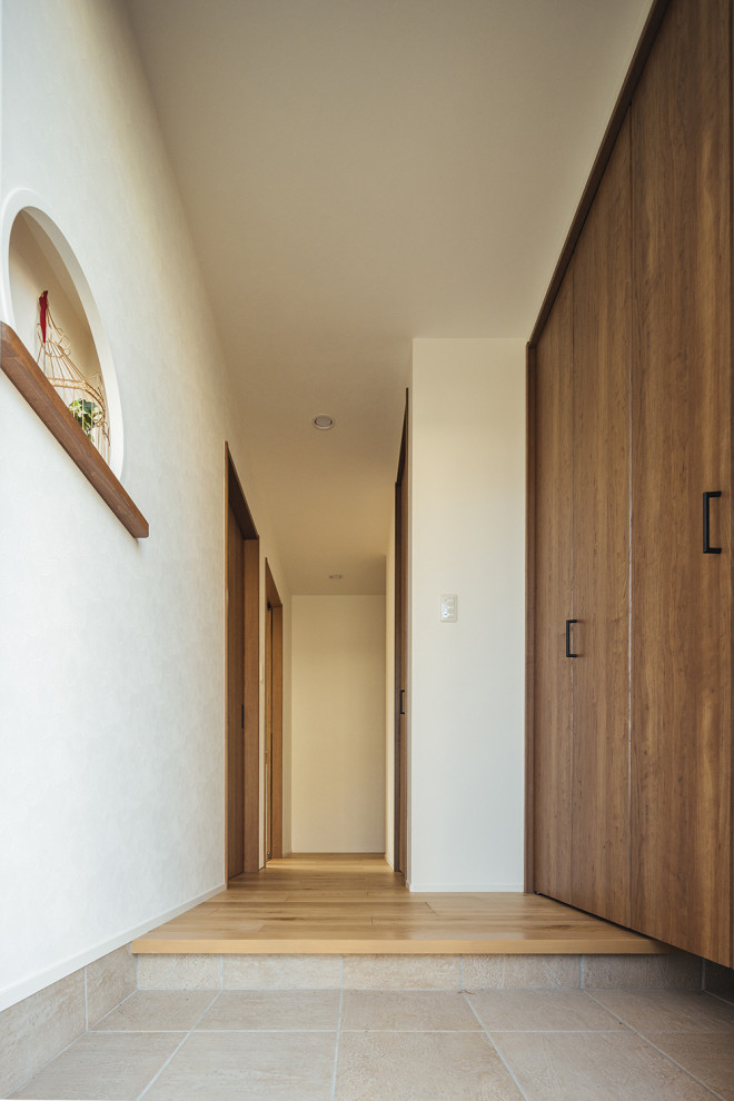 他の地域にある小さなおしゃれな玄関ニッチ (白い壁、磁器タイルの床、濃色木目調のドア、ベージュの床、クロスの天井、壁紙、白い天井) の写真